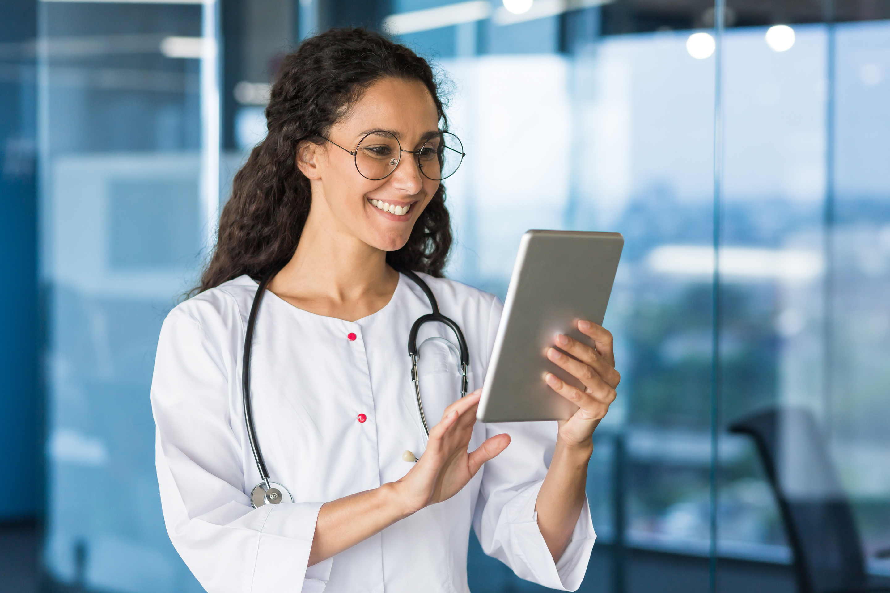 Latin American doctor woman using tablet computer, female doctor working inside office building wearing white medical coat